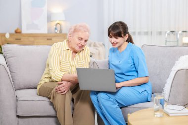 Huzurevinde yaşlı bir kadına dizüstü bilgisayar kullanmayı öğreten bakım işçisi.