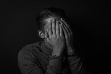 Kelepçeli adam yüzünü gizliyor. Yakalanan suçlu. Siyah ve beyaz tonlama