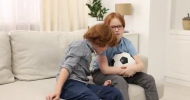 İki kardeş evdeki kanepede futbol topuyla oynuyorlar.