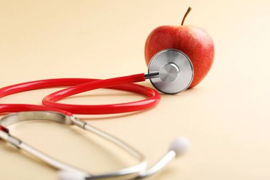Bej arka planda olgun elma ve steteskop, yakın plan.