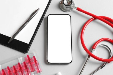 Sağlığınıza. Akıllı telefon, steteskop, pano, ampuller ve arka planda kalem, düz konum