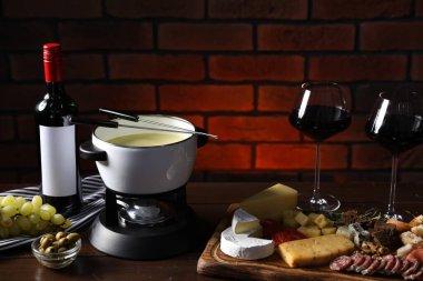 Erimiş peynir, şarap ve ahşap masada atıştırmalıklarla fondü tenceresi (caquelon)