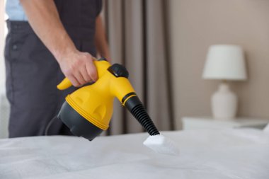 Haşere kontrol işçisi yatağı temizliyor, kapalı alanda buharlı temizleyiciyle, yakın plan. Metin için boşluk