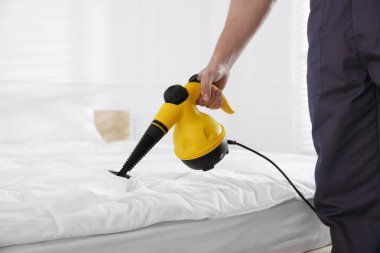 Haşere kontrol işçisi yatağı temizliyor, kapalı alanda buhar temizleyicisiyle, yakın plan
