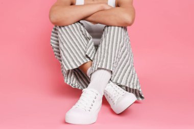 Pembe arka planda şık beyaz ayakkabılar giyen kadın, yakın plan.