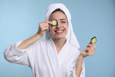 Havluya sarılı güzel bir kadın ve açık mavi arka planda salatalık dilimleri.