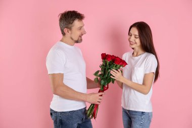 Pembe arka planda gül buketi olan mutlu bir çift. Sevgililer Günü kutlaması