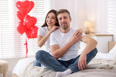 Yataktaki mutlu çift kalp şeklinde balonlarla süslenmiş. Sevgililer Günü kutlaması