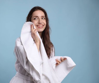 Güzel bir kadın açık mavi arka planda havluyla saçlarını kurutuyor.