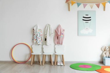 Oyun odasındaki ışıklı duvarda şık sandalyeler ve elbiseler asılı. İç tasarım