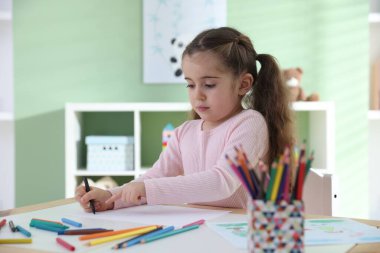 Masada pastel boyayla resim çizen sevimli küçük kız.