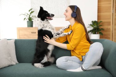 Evdeki kanepede sevimli köpeğiyle kulaklıklı, gülümseyen bir kadın.