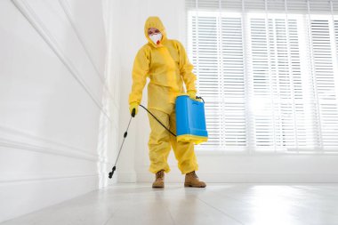 Koruyucu giysiler içinde böcek ilacı sıkan haşere kontrol görevlisi, düşük açılı.