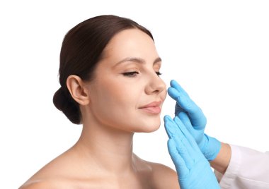 Doktor, estetik ameliyattan önce beyaz arka planda hastanın yüzünü kontrol ediyor.