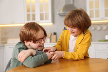 Şirin kardeşler mutfaktaki ahşap masada birlikte vakit geçiriyorlar.