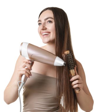 Gülümseyen kadın saçını saç kurutma makinesiyle şekillendiriyor ve beyaz arka planda tarıyor.