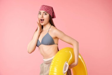 Pembe arka planda şişirilebilir yüzüğü olan mayolu ve pantolonlu sürpriz bir kadın.