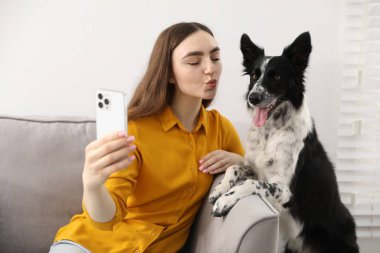 Sevimli köpeğiyle gülümseyen kadın evdeki kanepede selfie çekiyor.