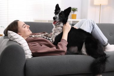Evdeki kanepede sevimli köpeğiyle gülümseyen kadın.