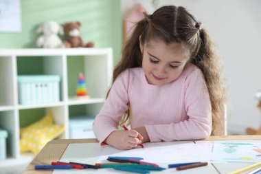 Masada pastel boyayla resim çizen sevimli küçük kız.