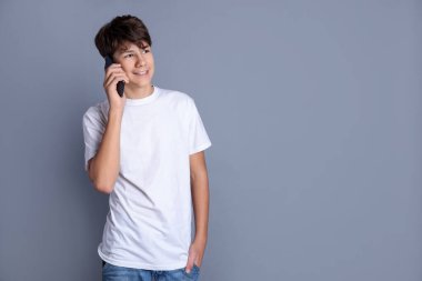 Akıllı telefondan konuşan genç çocuk gri arka planda, mesaj için yer var.