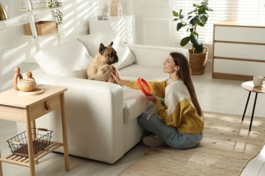 Şirin köpeği ve oyuncağıyla evdeki kanepenin yanında dinlenen bir kadın.