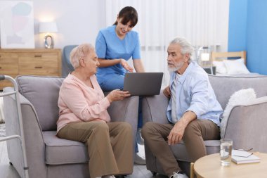 Bakım işçisi üst düzey erkek ve kadınlara huzurevinde dizüstü bilgisayar kullanmayı öğretiyor.