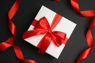 Güzel kırmızı kurdeleler ve koyu arkaplanda hediye kutusu, düz yatıyordu.