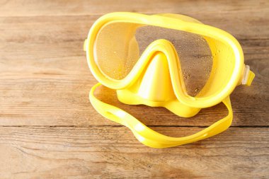 Tahta arka planda su damlaları olan sarı dalış maskesi, yakın plan. Metin için boşluk