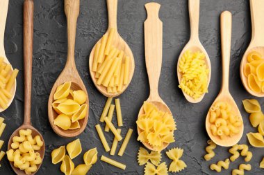 Tahta kaşıklardaki farklı çiğ makarna türleri siyah masada, düz yatıyordu.