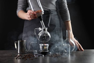 Gri masada vakumlu kahve makinesiyle kahve yapan kadın, yakın plan.