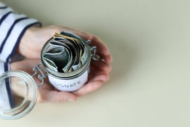 Bağış kavanozu ve bej arka planda dolar banknotları olan bir kadın. Metin için boşluk