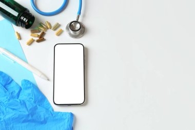 Sağlığınıza. Akıllı telefon, steteskop, tıbbi eldivenler, haplar ve arka planda kalem, düz yatak. Metin için boşluk