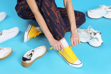 Açık mavi arka planda farklı spor ayakkabıları deneyen kadın, yakın plan