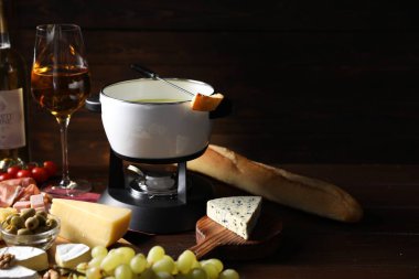 Erimiş peynir, şarap ve ahşap masada atıştırmalıklarla fondü tenceresi (caquelon)
