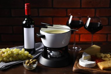 Erimiş peynir, şarap ve ahşap masada atıştırmalıklarla fondü tenceresi (caquelon)