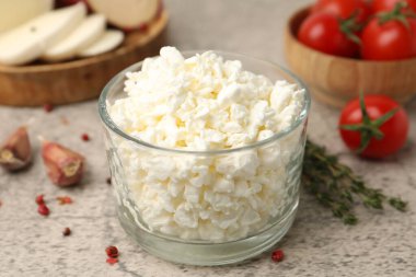 Cam kasede taze süzme peynir, gri masada domates ve baharatlar, yakın plan.