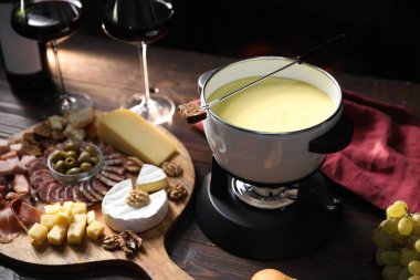 Nefis eritilmiş peynir fondü kabında, abur cuburlar ve bardaklar ahşap masada siyah arka planda, yakın plan