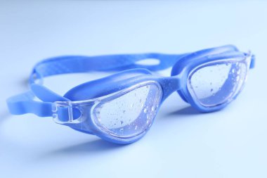 Açık mavi arkaplanda su damlaları olan yüzme gözlükleri, yakın plan