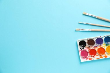Açık mavi arka planda suluboya palet ve fırçalar, düz. Metin için boşluk