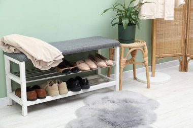 Ayakkabı bankı, farklı ayakkabılar, kıyafetler ve yeşil duvarın yanındaki bitki örtüsü.