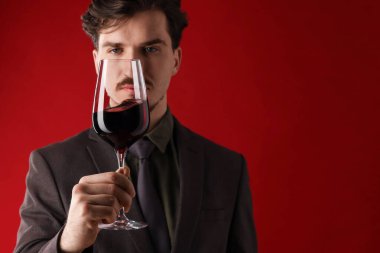 Profesyonel şarap garsonu kırmızı arka planda şarap tadıyor.