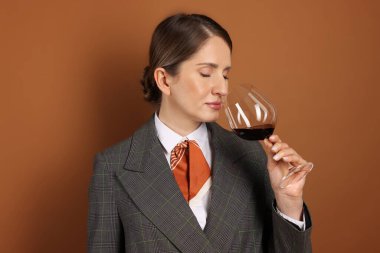 Profesyonel şarap garsonu kahverengi arka planda şarap tadıyor.