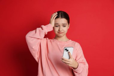 Kırmızı arka planda akıllı telefon kullanan genç kız.