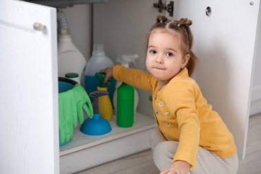 Evde çocuk güvenliği. Küçük kız mutfakta temizlik malzemeleriyle oynuyor.