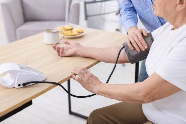 Bakıcı evde yaşlı kadının kan basıncını ölçüyor, yakın plan.