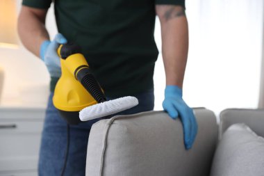 Haşere kontrol işçisi kanepeyi temizliyor. Kapalı alanda buhar temizleyicisi var.