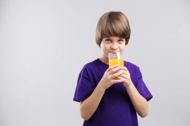 Açık gri arka planda bir bardak taze portakal suyu olan çocuk. Metin için boşluk