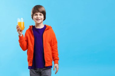 Açık mavi arka planda bir bardak taze portakal suyu olan çocuk. Metin için boşluk