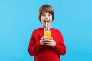 Açık mavi arka planda bir bardak taze portakal suyu olan çocuk.